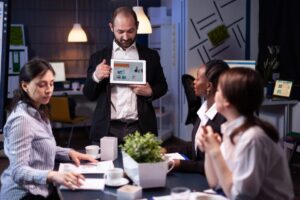 A group of professionals engage in a meeting, with one person presenting data on a tablet while others listen attentively.