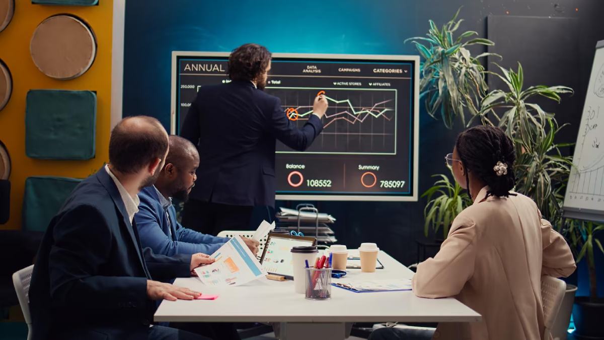 A professional meeting with participants discussing a data analysis presentation on a large screen, featuring graphs and statistics.