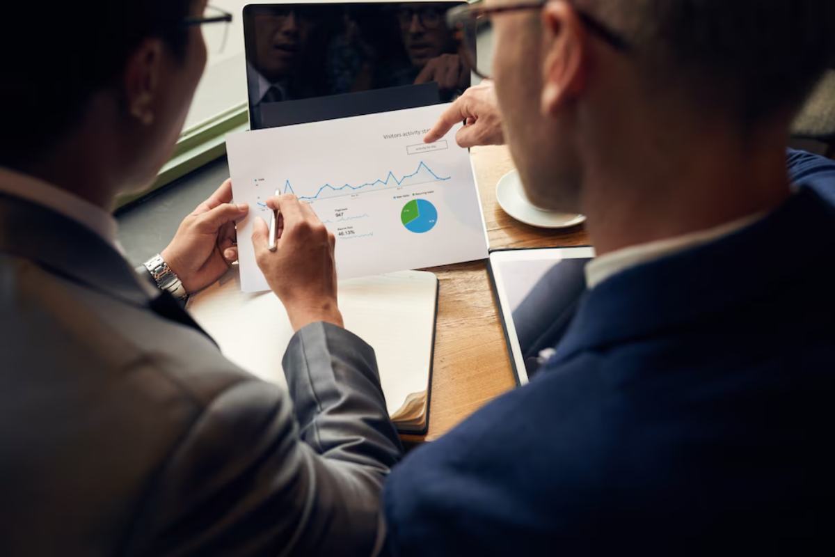 Two professionals discuss a report featuring a line graph and pie chart on a wooden table